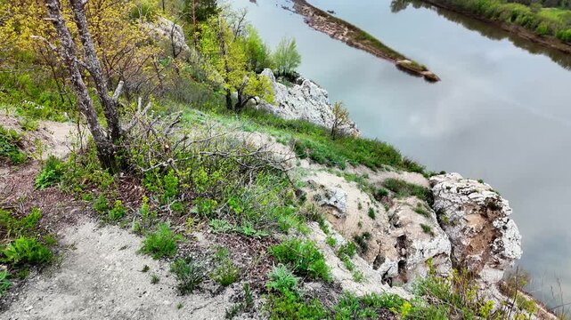Limestone cliff overlooking river island and floodplain with sheer white rock face, trees clinging to edge, winding channel and distant patchwork fields under brooding sky