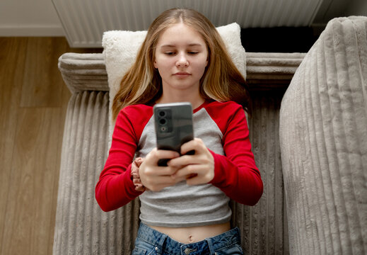 Girl Watching Movie On Smartphone With Headphones While Lying On The Couch