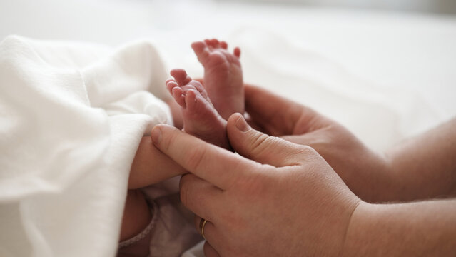 A pair of tiny newborn feet rests gently in the hands of an adult. Soft surroundings create a warm atmosphere.