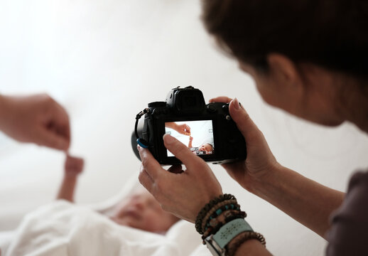 Woman Takes Pictures Of Newborn Baby While Mom Holds Baby Hand. Bright And Warm Setting.