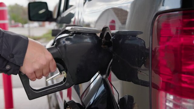 A close-up shot of hand pulling out gasoline nozzle from car tank at gas station and closing cap, motion clip.