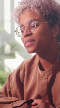 The content creator waves a friendly goodbye or hello to her digital audience. Her warm smile and stylish glasses highlight the personal connection she builds through her online videos.