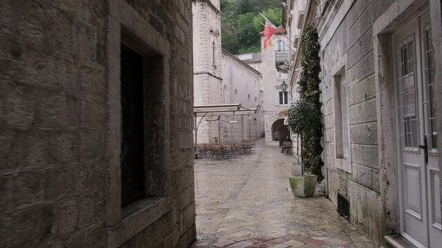 Narrow historic alley paved with stone tiles, surrounded by old stone buildings leads to The Cathedral of Saint Tryphon in Kotor, Montenegro
