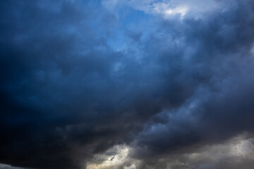 Obraz premium Dramatic dark storm clouds filling the sky with brooding blue-grey tones and glimpses of light breaking through below