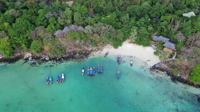 Phi Phi Island, Thailand : Aerial drone footage of long tail boats by white sand beach in front of jungle resorts in Ko Phi Phi Don of Bangkok, Thailand. Taken with tilt down motion