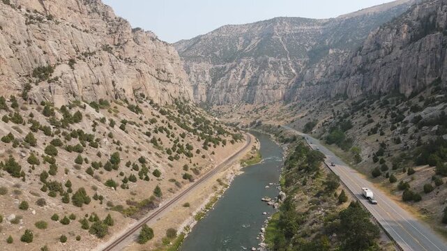 Cinematic drone shot ascending and moving forward through the majestic Wind River Canyon in Wyoming. High-quality 1080p 30fps footage captures the scenic river, a highway with a semi-truck driving by.