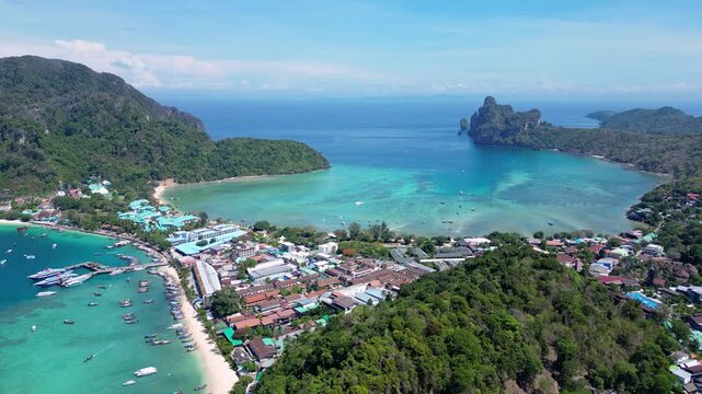 Phi Phi Island, Thailand : Aerial backward drone footage of jetty in Phi Phi Island with seafront resorts and limestone cliff and boat in the with dramatic sky in the Andaman sea in Krabi province.