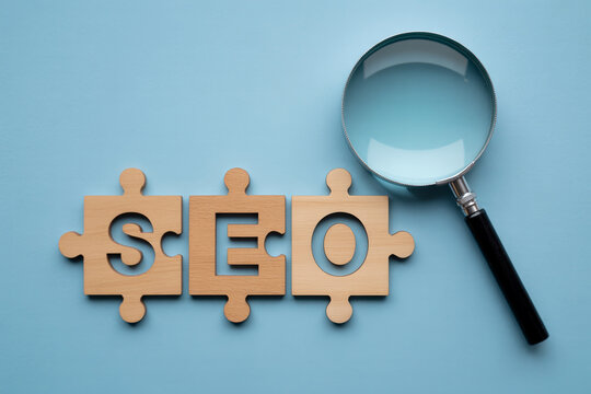 SEO concept with wooden puzzle pieces and magnifying glass on blue background