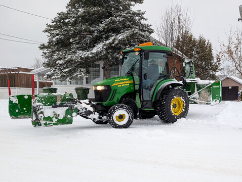 Canada, 01 April 2026 : John Deere tractor operated by Paul Tremblay clears snow with a Normans snowblower in a residential area during winter