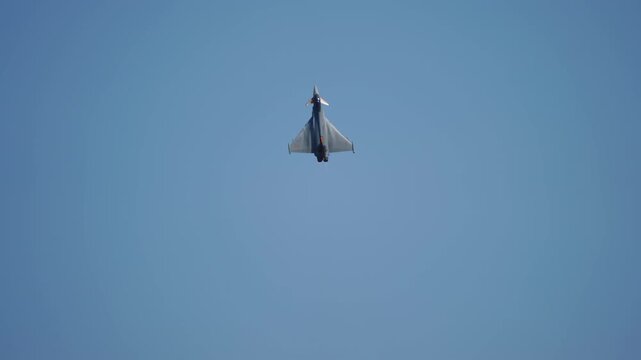 A delta-wing canard military fighter jet is seen from directly below climbing near-vertically against a clear blue sky, its triangular planform filling the frame