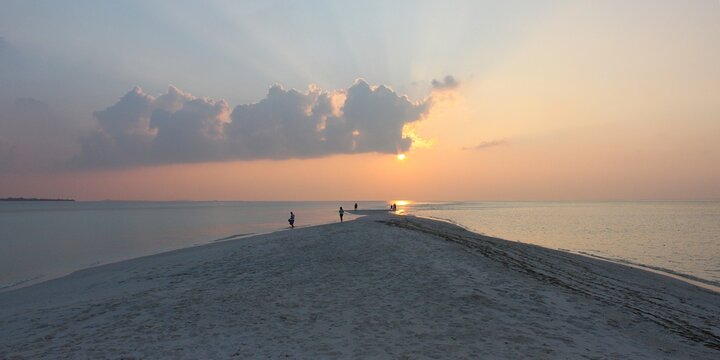 Stunning sunset over tropical sandbank island in Maldives with calm ocean water under dramatic evening sky, spectacular serene nature landscape view for luxury travel resort holiday vacation.