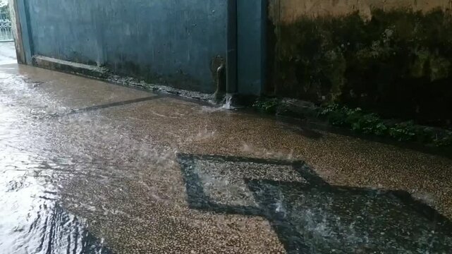 Heavy rain water flowing from pipe on wet street asphalt background.