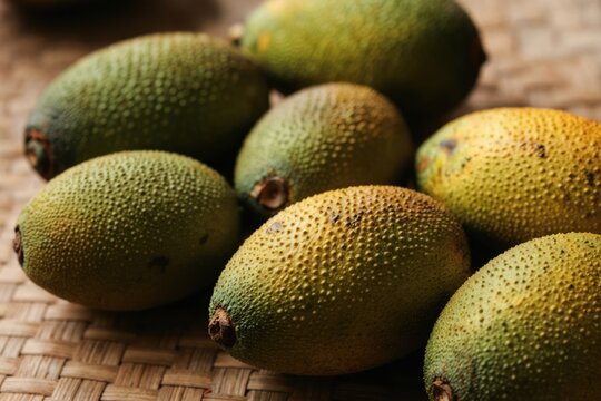 Ripe Macauba fruits lay on woven surface. The spiky green and yellow fruits show natural texture and color variation. Ready for harvest and consumption.