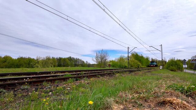 Low angle video shot of a vintage blue and red EL2 Krokodyl electric locomotive moving on railway tracks with raised pantograph, passing through a green landscape under a cloudy sky.