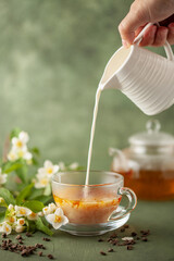 Composition with cup of jasmine milk tea and flowers on green background