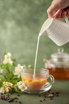 Composition with cup of jasmine milk tea and flowers on green background