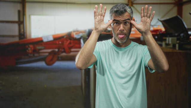 Man posing with hands raised near face and tongue out beside orange airplane in airport; playful silliness.