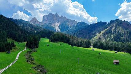 Majestic mountain range rises over lush green pastures under a bright blue sky with fluffy clouds in a serene landscape © Tetiana