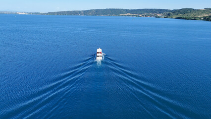 Fototapeta premium Serenity in motion as a lone boat glides across the tranquil blue waters under the sunlit sky of a beautiful afternoon