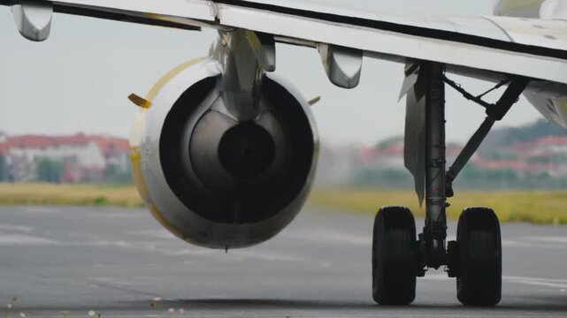 Extreme close-up of a commercial jet engine intake with distinctive yellow nacelle rim and the main landing gear with dual wheels rolling on the runway