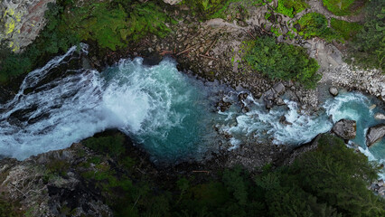 Rushing river cascades over rocky terrain in a lush green landscape under a bright blue sky during the afternoon © Tetiana