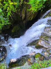 Water cascades gracefully over moss-covered rocks in a serene forest, capturing the essence of nature's tranquility during a sunny afternoon © Tetiana