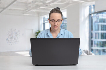 Fototapeta premium Focused businesswoman working on laptop in modern office interior, symbolizing concentration, remote work and digital productivity