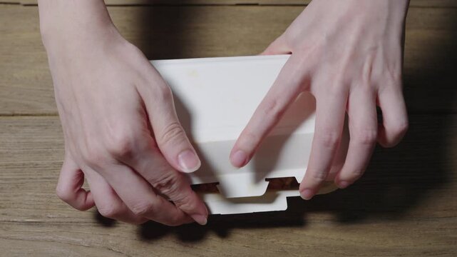 Delicious American fried rice served in a white paper takeout container on a rustic wooden table. The meal includes a sunny-side-up fried egg, ham slices, grilled sausages, and raisins mixed into rice
