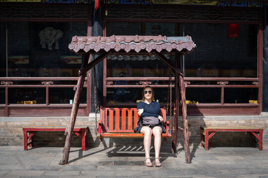 Woman sitting on a traditional wooden swing in front of an ancient Chinese building