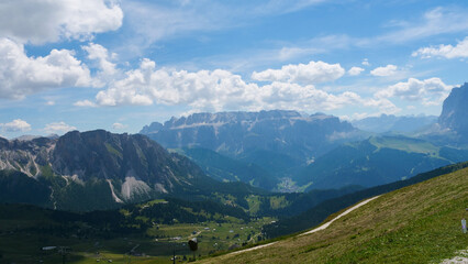 Fototapeta premium Majestic clouds embrace the Dolomites as sunlight dances over lush valleys and rugged peaks during a crisp summer afternoon
