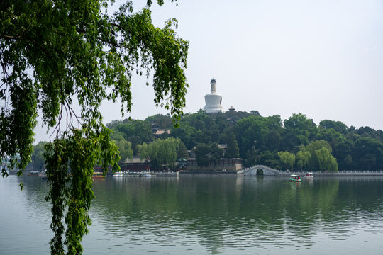 White Dagoba atop lush green hill overlooking a serene lake in Beijing