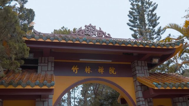 Beautiful stone entrance gates to the Truc Lam Zen Monastery in Da Lat, Vietnam with Chinese letters and its walls painted in orange color with traditional tiled roof and Dharmachakra or Wheel of Life