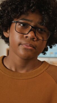 Vertical close-up portrait of young curly African American male student in nerdy glasses blowing dusting off forgotten textbook to return back to school after vacation or summer holidays