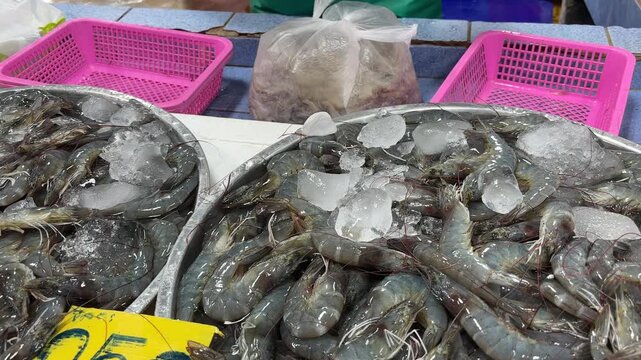Close-up of raw grey shrimp displayed on a metal tray with ice at a busy Asian seafood market, capturing the process of buying fresh shrimp in a local market setting.