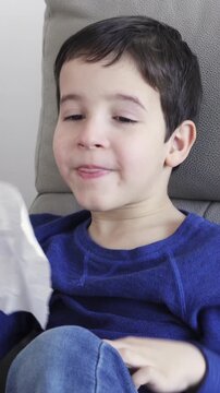 Child blowing in a wipe suffering flu symptoms sitting on a sofa at home in winter