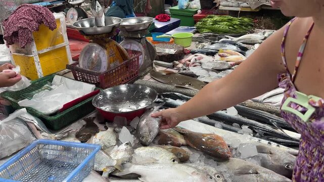 Close-up shot of a bustling fish market stall, showcasing a variety of freshly caught fish displayed on ice.  The scene demonstrates the lively atmosphere of a traditional seafood market.