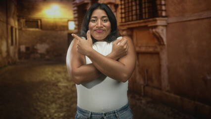 Naklejka premium Woman crossing arms over chest showing forearms and pointing fingers in a narrow cobblestone alley at night; confidence.