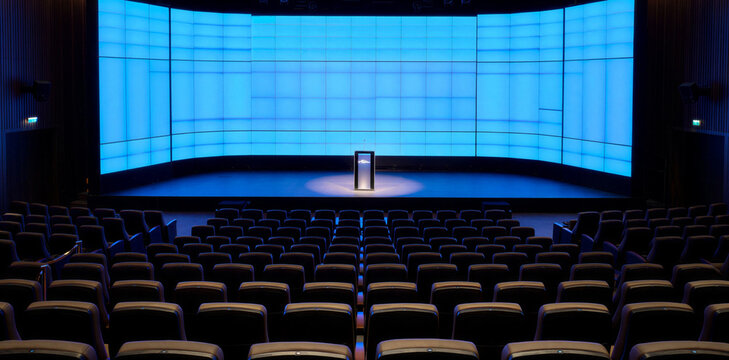 Spacious empty conference theater hall featuring large digital blue background screen and rows of comfortable seats for presentations and corporate business events or lectures