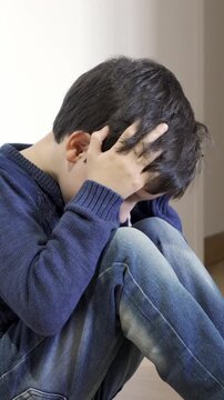 Upset problem child with head in hands sitting on floor concept for bullying, depression stress or frustration at home