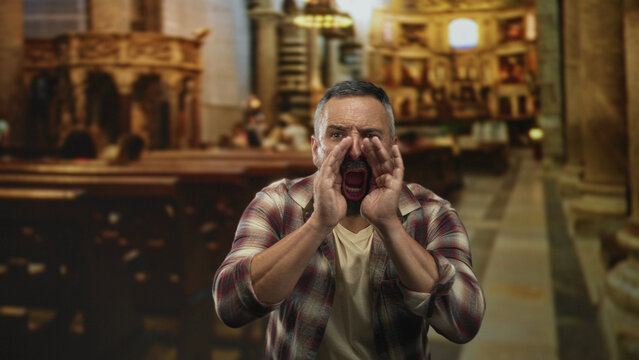 Man cupping hands around mouth shouting toward the nave in a church aisle beside wooden pews and stone pillars; anger protest.