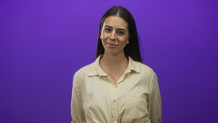 Fototapeta premium Woman brunette with head tilt and slight smile showing face and neck in studio with purple backdrop; confidence casual ease.