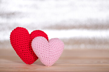Fototapeta premium Red and pink crocheted hearts standing on a wooden surface against a blurred light background.