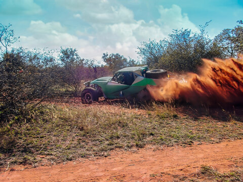 Green off-road racing buggy kicking up dust on a dirt track sparse green bushes and trees