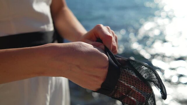 Glove hands sea woman puts on black lace gloves while standing by the ocean with sunlit bokeh water