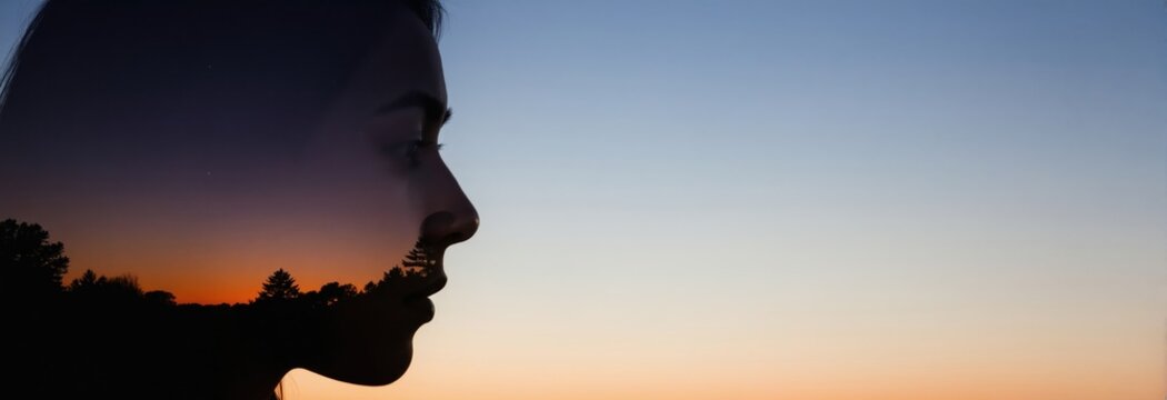 Double exposure profile silhouette of woman head against colorful sunset sky. Inside her head is a forest landscape with trees. This represents thoughts.