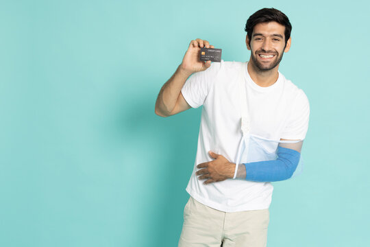An injured male patient wearing a cervical neck brace and arm sling holds a credit card, isolated on a cyan background. Perfect for medical billing, health insurance, and payment concepts