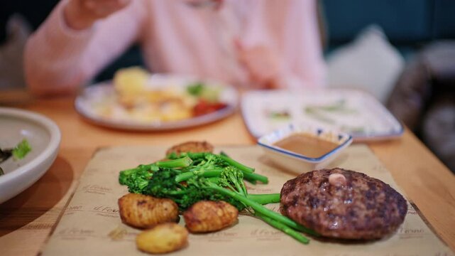 A cooked burger patty is placed on a serving board alongside vegetables such as broccoli and small roasted potatoes