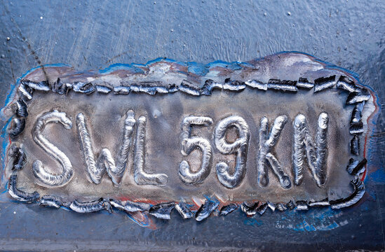 Swl 59kn safe working load marking welded on steel plate of a ship or industrial equipment close up