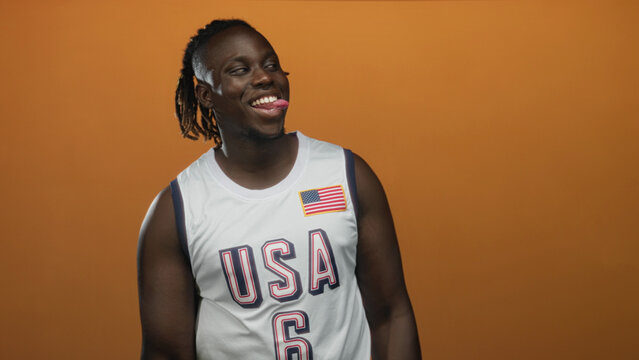Man smiling with tongue out wearing usa basketball jersey with american flag patch in orange studio; playful.