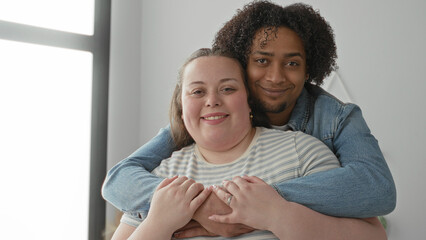 Obraz premium Woman embraced from behind by man, smiling, hands clasped over chest in studio; affection contentment.